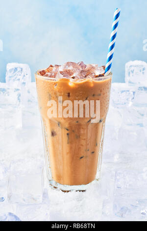 Boisson d'été à la crème de café de glace dans un grand verre avec des gouttelettes et de paille entouré par des cubes de glace sur la neige sur fond bleu. Copie, Selective focus Banque D'Images