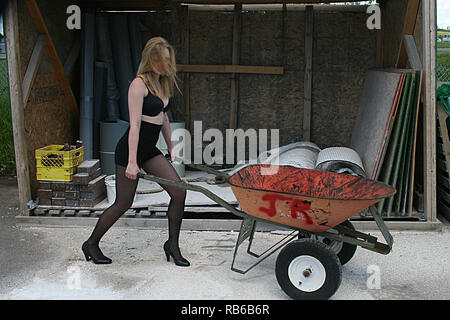 Blond Woman wearing bas de nylon, talons hauts et mini shorts en poussant une brouette Banque D'Images