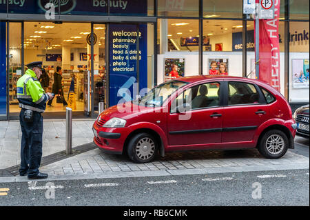 Le Directeur de la Circulation et Stationnement Enforcer émet un billet à une voiture stationnée illégalement dans la ville de Cork, Irlande. Banque D'Images