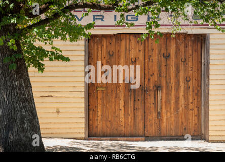 Un grand lit en bois avec porte de protection flexible joint plusieurs chaussures, sur le côté de la rue, au soleil, avec un arbre en premier plan Banque D'Images