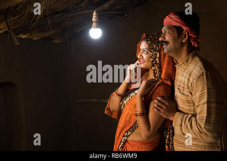 Couple Indien Rural enchanté à la lueur de l'ampoule électrique et de l'électricité d'atteindre leur maison après une longue attente Banque D'Images
