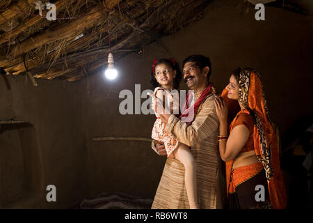 La famille de l'Inde rurale enchanté à la lueur de l'ampoule électrique et de l'électricité d'atteindre leur maison après une longue attente Banque D'Images