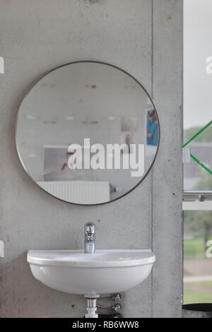 Lavabo et miroir circulaire contre mur en béton dans l'espace commun à l'étage supérieur du studio building. Les Ballets C de la B studio building, Gent, Belgique Banque D'Images