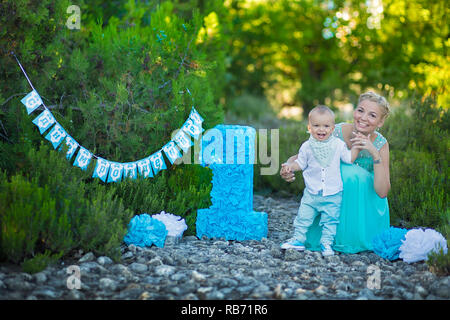 Belle mère dame maman en robe bleue élégante avec son fils et un numéro anniversaire en parc. Banque D'Images