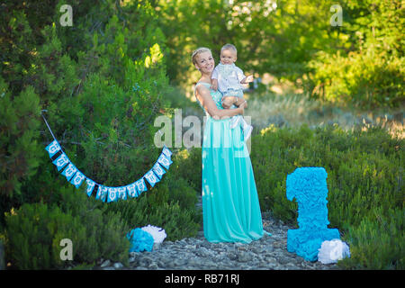 Belle mère dame maman en robe bleue élégante avec son fils et un numéro anniversaire en parc. Banque D'Images