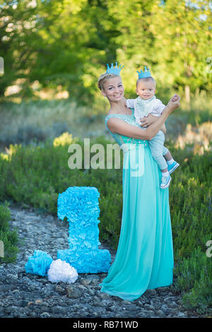 Belle mère dame maman en robe bleue élégante avec son fils et un numéro anniversaire en parc. Banque D'Images