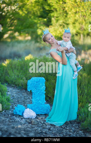 Belle mère dame maman en robe bleue élégante avec son fils et un numéro anniversaire en parc. Banque D'Images