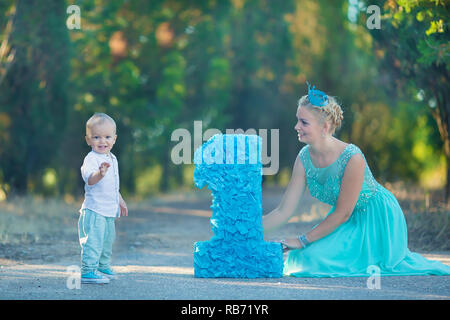 Belle mère dame maman en robe bleue élégante avec son fils et un numéro anniversaire en parc. Banque D'Images