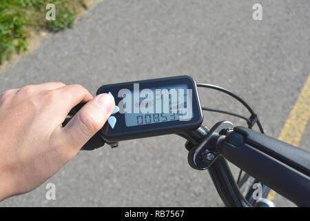 Un homme part appuie sur un bouton d'un scooter électronique noir location. Ordinateur de vélo installé sur un guidon de vélo. L'homme en appuyant sur un bouton sur l'e-bike Banque D'Images