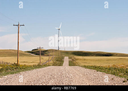 Éolienne et ligne électrique le long d'une route de gravier dans un paysage de prairie Banque D'Images