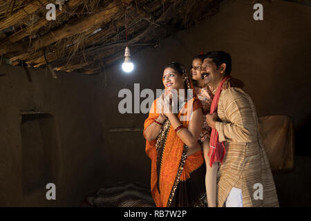 La famille de l'Inde rurale enchanté à la lueur de l'ampoule électrique et de l'électricité d'atteindre leur maison après une longue attente Banque D'Images