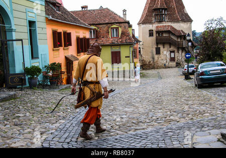 Homme habillé en costume de l'archer médiéval va sur une des rues aux maisons colorées à Sighisoara, Roumanie. Banque D'Images