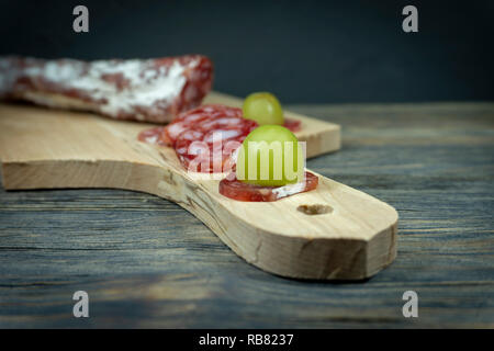 Raisin vert frais tranchés sur la tranche de Saucisson Fuet salés à sec le manche d'une planche à découper en bois Banque D'Images