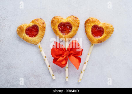 Tarte aux fraises en forme de coeur pop sur un bâton pour la Saint-Valentin. Décorée avec un ruban rouge. Banque D'Images