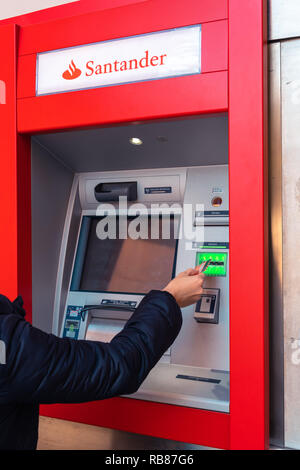 Jeune femme mettant en carte de débit à un guichet automatique de la Banque Santander, l'une des plus grandes banques espagnoles. Distributeur automatique de retrait d'espèces. La main de femme. Visa, Mastercard. Banque D'Images