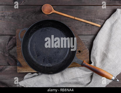 Tôle ronde noire avec poignée en bois et une cuillère de bois sur une table brune, vue du dessus Banque D'Images