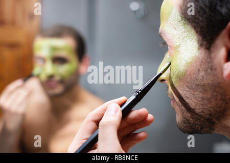 Attractive male à l'aide de crème de beauté produit pour la santé de la peau. Concept de costumes, cosmétiques, bien-être, des traitements topiques et maquillage. Les jeunes gay homme blanc s'applique un masque d'avocat sur le visage pour les soins de la peau. Banque D'Images