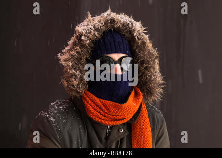 Portrait d'un homme portant un aventurier hiver chaud manteau vert avec la fourrure capot, une casquette bleu, un foulard orange et noir lunettes style rétro Banque D'Images