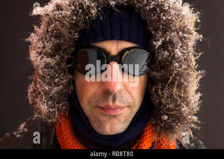 Portrait d'un homme portant un aventurier hiver chaud manteau vert avec la fourrure capot, une casquette bleu, un foulard orange et noir lunettes style rétro Banque D'Images