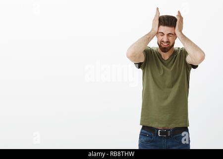 Portrait d'un homme souffrant d'énormes maux de tête migraine ou attraper avec les deux mains en plissant les yeux de douleur et de détresse d'être contrarié et stressés debout sur fond blanc mécontent Banque D'Images