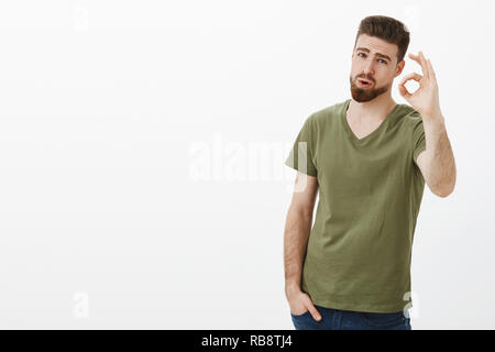 Wow nice shot, impressionnant. Portrait of attractive cool et élégant barbu en t-shirt d'être stupéfié avec grand travail d'ami montrant bien l'effort magnifique geste check out de l'approuver sur mur blanc Banque D'Images