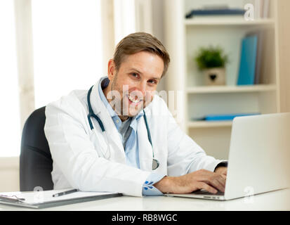 Portrait of happy young médecin en blouse blanche qui travaillent sur un ordinateur portable et de la paperasserie dans l'hôpital clinique de 24 pour les soins de réussite professio Banque D'Images