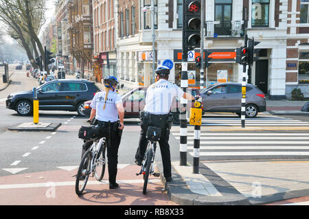 Les agents de police néerlandais (politie) sur l'attente de patrouille à vélo aux feux de circulation, Amsterdam, Hollande du Nord, Pays-Bas Banque D'Images