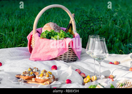 Pique-nique dans la forêt sur sunny meadow, couverture, panier en osier, verres à vin, Bruschetta de fromage et de poire, des collations, des fruits, des pommes, du pain. Concept de Banque D'Images