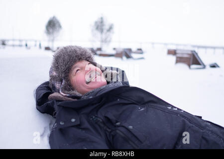 Bel homme senior dans des vêtements chauds et un chapeau allongé sur la neige et de rêve s'amusant Banque D'Images