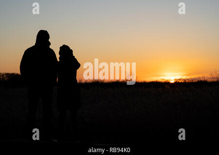 Silhouette d'un couple standing et regarder le coucher du soleil Banque D'Images