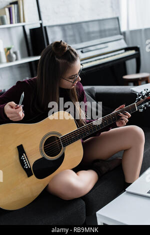 Girl sitting on couch, jouer de la guitare et la tenue conjointe de la marijuana dans la salle de séjour Banque D'Images