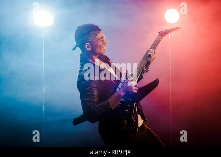 Heureux homme rock star veste en cuir en effectuant sur guitare électrique sur scène avec la fumée et l'Éclairage dramatique Banque D'Images