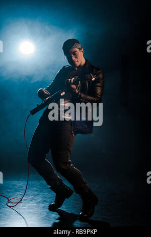 Rock star masculine concentrées en blouson de cuir sur l'exécution de la guitare électrique sur scène avec de la fumée et de projecteur Banque D'Images