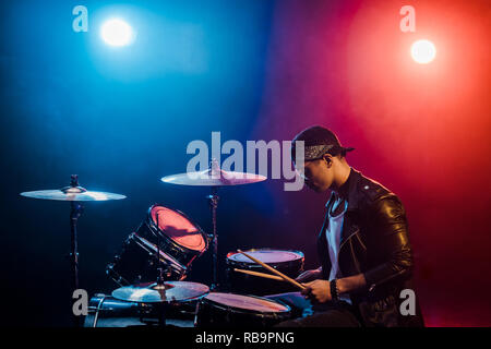Veste en cuir homme musicien à jouer de la batterie lors de concert de rock sur scène avec de la fumée et des projecteurs Banque D'Images