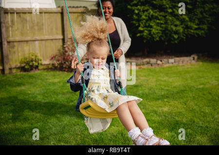 Petite fille s'amuser tout en étant poussé sur une balançoire par sa mère. Banque D'Images