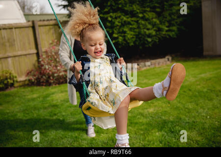 Petite fille s'amuser tout en étant poussé sur une balançoire par sa mère. Banque D'Images
