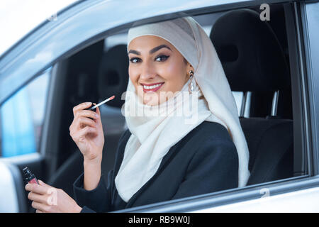 Beautiful smiling young woman sitting in car musulmane et la tenue d'un brillant à lèvres Banque D'Images