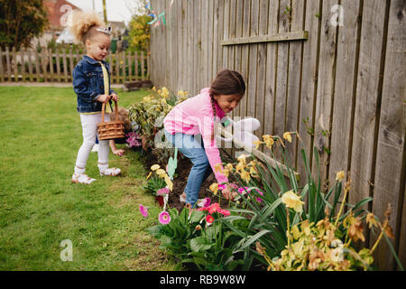 Deux petites filles à la recherche d'oeufs de pâques en chocolat dans le jardin. Ils sont à la recherche dans le lit de fleur, à côté les jonquilles. Banque D'Images