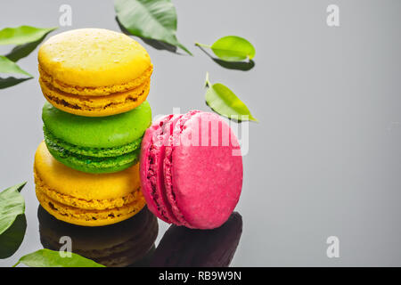 Différentes couleurs douces Gâteau dessert français macarons macarons sur fond gris foncé décoré de feuilles vertes copy space Banque D'Images