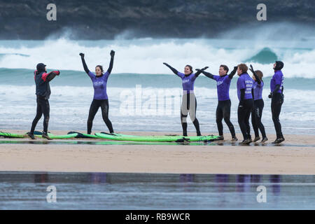 Les surfeurs débutants se réchauffer avec leur moniteur au début d'une leçon de surf à la plage de Fistral Newquay en Cornouailles. Banque D'Images