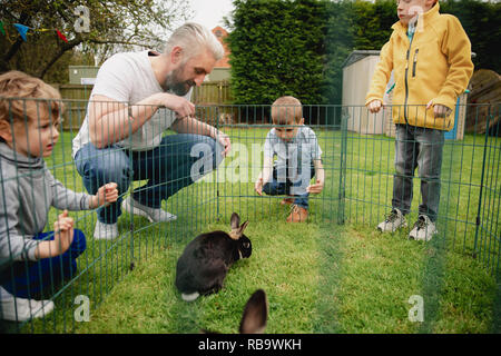 Groupe d'enfants à genoux en plein air à côté d'une plume de lapin. Ils essaient de caresser les lapins en mettant leurs doigts dans les trous de la clôture. Banque D'Images