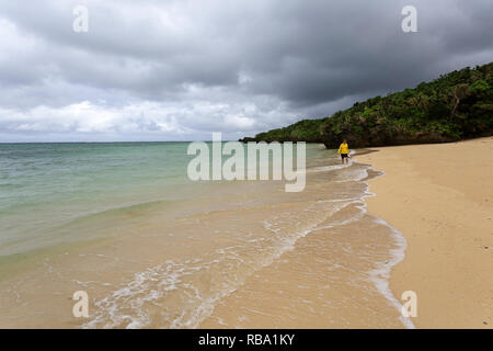 Jeune femme en veste jaune debout, marcher dans l'eau peu profonde sur une belle plage isolée, Ishigaki, Japon Banque D'Images