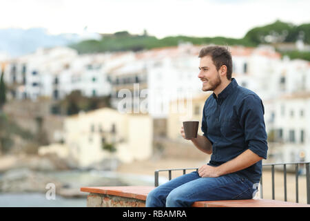 Homme heureux de boire du café et à l'écart assis sur une corniche dans une autre ville en vacances Banque D'Images