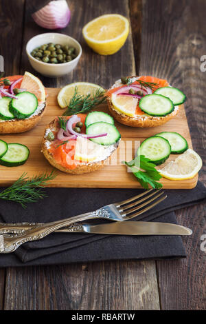 Sandwiches au saumon fumé, oignons rouges, câpres, de concombre et de citron sur fond de bois rustique Banque D'Images