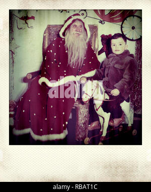 Photographie d'un petit garçon sur un cheval à bascule à côté de Santa Claus Banque D'Images