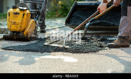 Portrait de deux travailleurs d'organiser l'asphalte frais avec les râteaux et pelle pour apaiser un bosse dans la route avec des machines à leur côté. Banque D'Images