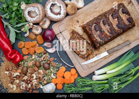 Rôti de noix vegan / pain de noix sur une planche en bois avec des ingrédients et un couteau de cuisine vintage à partir de ci-dessus. UK Banque D'Images