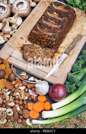 Rôti de noix vegan / pain de noix sur une planche en bois avec des ingrédients et un couteau de cuisine vintage à partir de ci-dessus. UK Banque D'Images