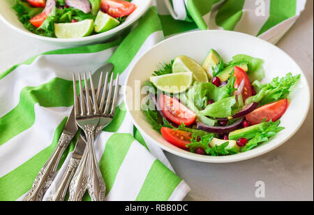 Frais sain salade avec tomates, d'avocat et de grenade dans des bols sur fond de béton léger. Banque D'Images