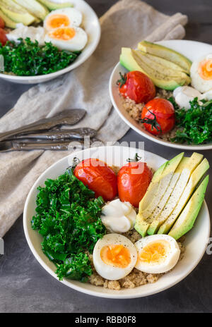 Le quinoa cuit avec des bols de bouddha les tomates, l'avocat, le chou vert, œufs durs et du yaourt grec sur fond de béton gris. Petit déjeuner sain. Focus sélectif. Banque D'Images